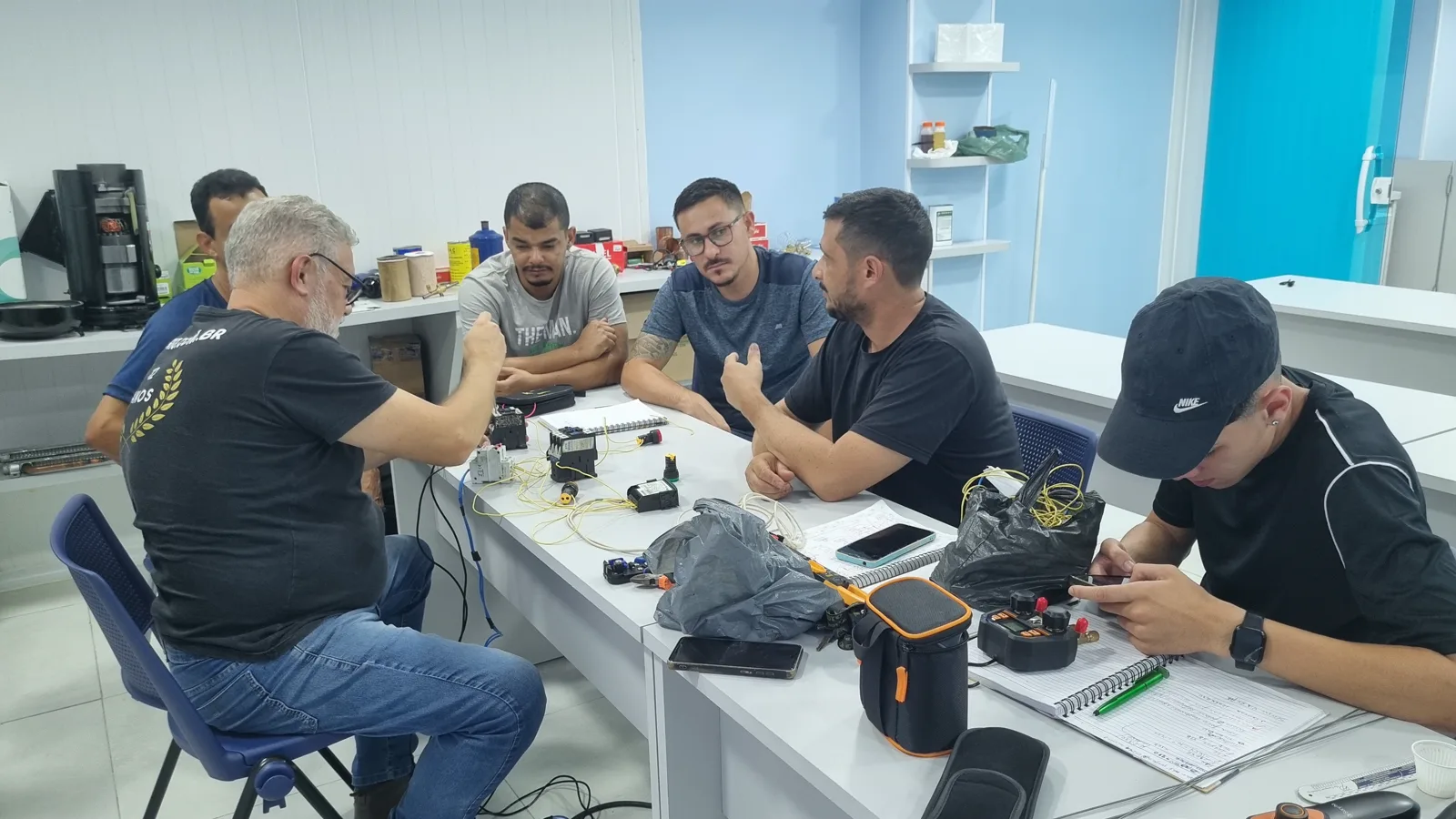 Instrutor orientando um grupo durante uma atividade prática com componentes elétricos
