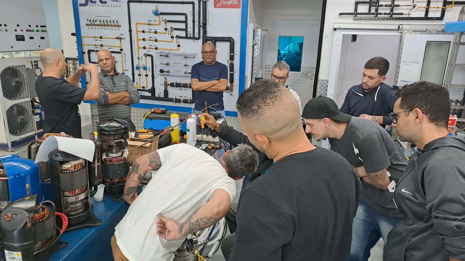 Turma acompanhando uma demonstração prática com componentes de refrigeração